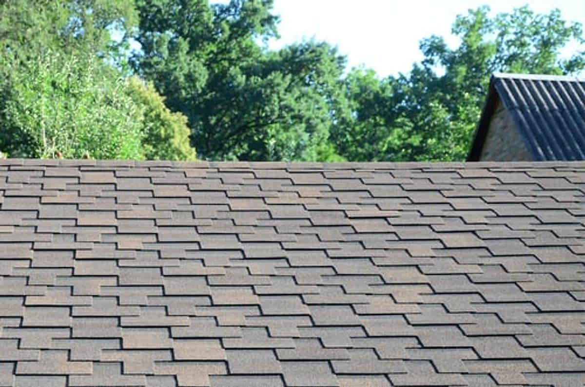 Aging grey asphalt shingle roof on a Kansas home surrounded by mature trees