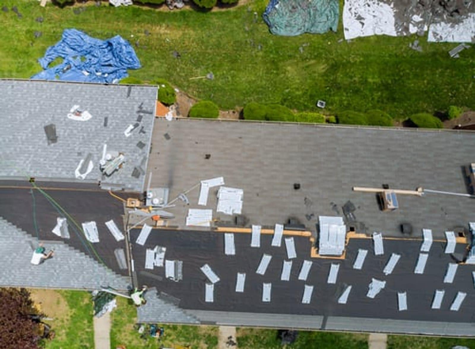 Aerial view of a shingle roof mid-repair with tarps and replacement materials laid out, Wichita, Kansas